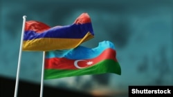 Armenian and Azerbaijani flags flutter in the wind against the evening sky.