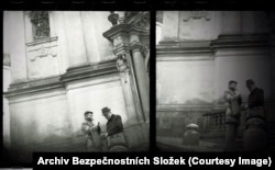 Пражский градтағы шіркеудің қасында сөйлесіп тұрған екі адамның жасырын камерамен түсірілген суреті.