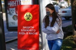 Коронавирустан қорғану жайлы баннер маңынан өтіп бара жатқан қыз.