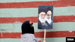 زنی در حال حمل عکس های آیت الله خمینی و خامنه ای در مراسم روز ۱۳ آبان - سالروز اشغال سفارت آمریکا در تهران- که از سوی جمهوری اسلامی «روز ملی مبارزه با استکبار» لقب گرفته است.